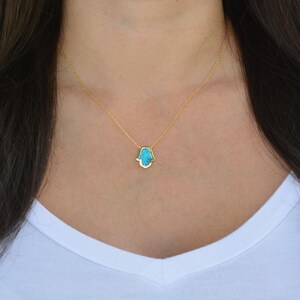 Peut inclure: Un collier en cha&icirc;ne dor&eacute;e avec un pendentif main de Hamsa en opale bleue.