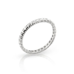 May include: A silver ring with a continuous row of small, clear gemstones. The ring has a delicate, detailed design around the band, and is set against a white background.
