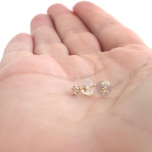 May include: A pair of gold stud earrings with a small clear stone in the centre. The earrings are on a white background.