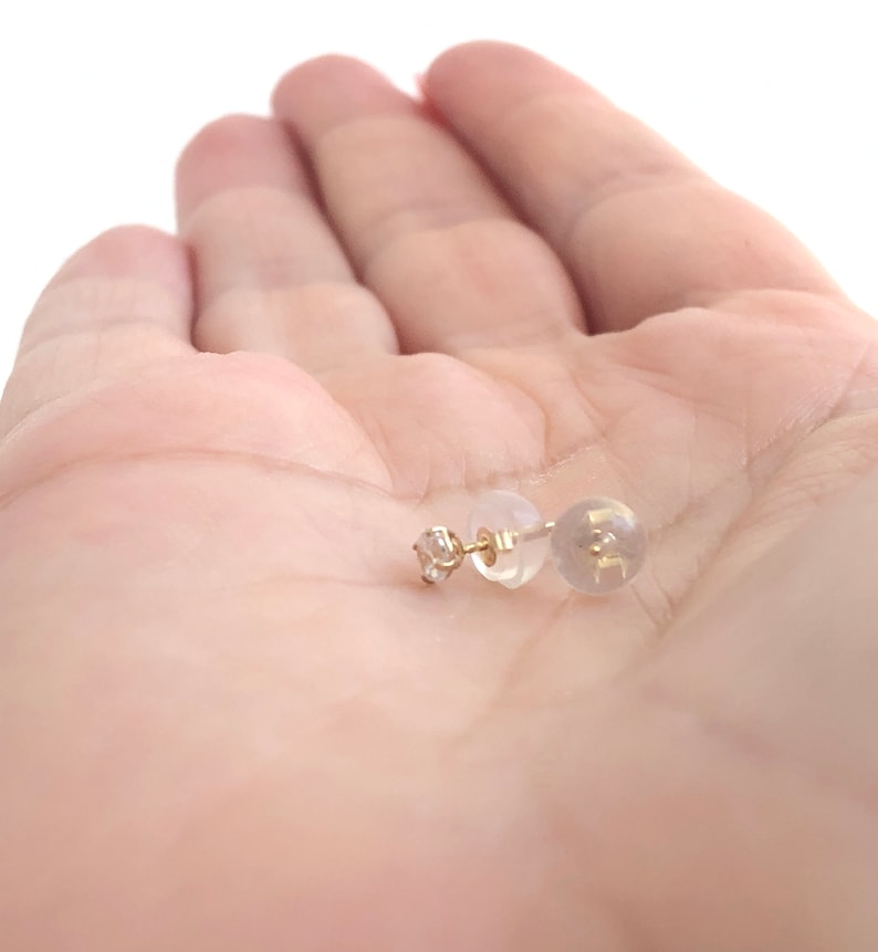 May include: A pair of gold stud earrings with a small clear stone in the centre. The earrings are on a white background.