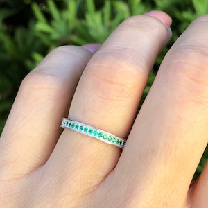 May include: A thin silver band ring with a row of small green gemstones.