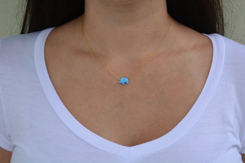 May include: A gold chain necklace with a small blue opal elephant pendant.