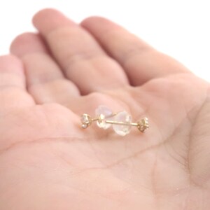 May include: A pair of gold stud earrings with small clear gemstones. The earrings are on a white background.