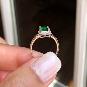 Puede incluir: Un anillo de plata con una esmeralda verde rodeada por un halo de diamantes m&aacute;s peque&ntilde;os.