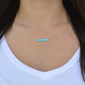 May include: A silver chain necklace with a thin bar pendant made of blue opal.