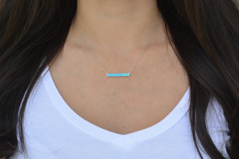 May include: A silver chain necklace with a thin bar pendant made of blue opal.