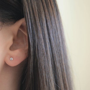 May include: A close-up of a person's ear with a small, clear diamond stud earring.