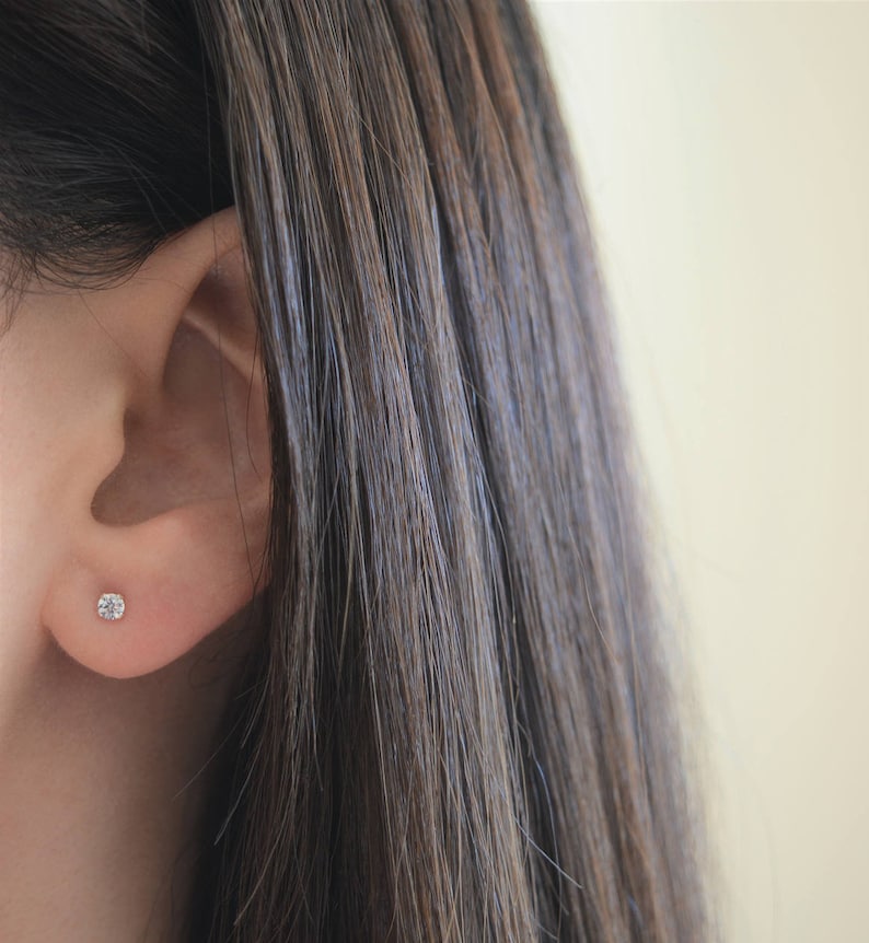 May include: A close-up of a person's ear with a small, clear diamond stud earring.