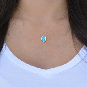 Peut inclure: Un collier en cha&icirc;ne dor&eacute;e avec un pendentif en forme de main de Hamsa turquoise.