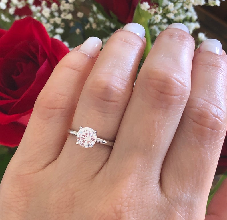 May include: A silver solitaire engagement ring with a round, clear diamond set in a simple band.