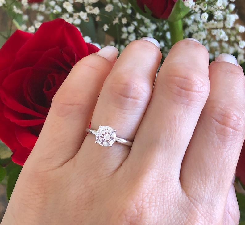 May include: A silver ring with a round, clear diamond set in the center.