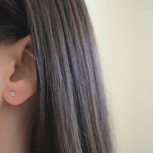 May include: A close-up of a person's ear with a small, clear diamond stud earring.