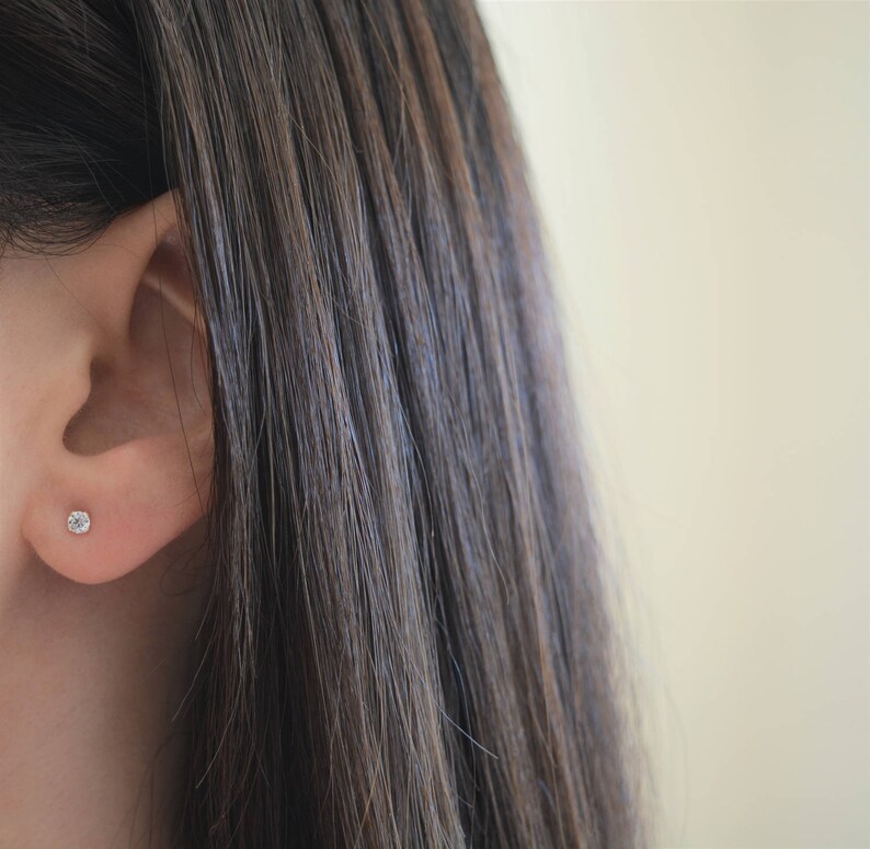 May include: A close-up of a person's ear with a small, clear diamond stud earring.