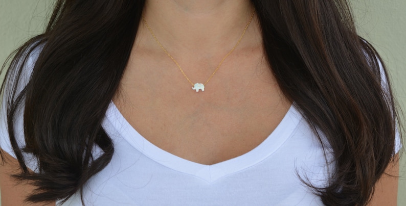 May include: A delicate gold chain necklace with a small white opal elephant pendant.