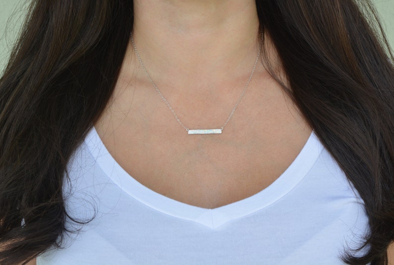 May include: A silver bar necklace worn by a model in a white top.