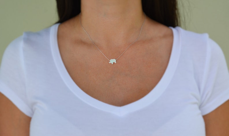 May include: A silver chain necklace with a small, white opal elephant pendant.