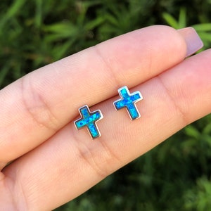 May include: A pair of silver cross earrings with blue opal stones.