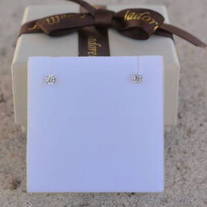 May include: A pair of diamond stud earrings displayed on a white card, with a brown gift box in the background.