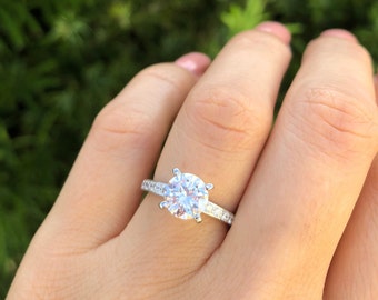May include: A silver engagement ring with a large, round, clear center stone and a band of smaller, clear stones.