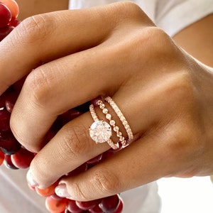 以下が含まれることがあります： 小さなダイヤモンドがセットされた、3つのローズゴールドのリング。中央のリングには、より大きな丸いダイヤモンドがセットされています。