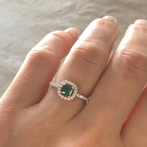 May include: A silver ring with a square green gemstone surrounded by smaller clear gemstones.
