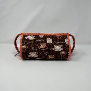 May include: A brown quilted makeup bag with a zipper closure. The bag is decorated with a pattern of coffee cups and the words "Espresso", "Latte", "Cappuccino", "Mocha", and "Caffe".