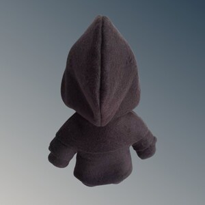 May include: A dark grey hooded cloak, seen from the back, featuring a pointed hood and small sleeves. The cloak is made of a soft, textured fabric. The background is a grey and blue gradient.