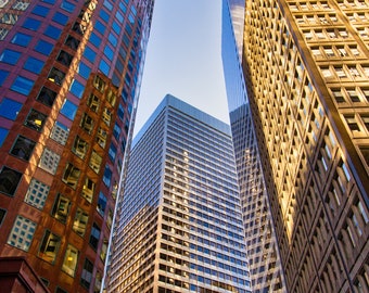 May include: Three tall buildings with glass windows, one is brown, one is silver, and one is gold. The buildings are against a blue sky.