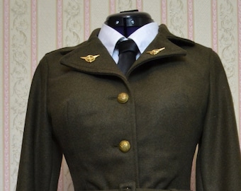 Op de afbeelding: Een donkergroene militaire jas en rok set met gouden knopen en een riem. De jas heeft een kraag en lange mouwen. De rok is knielengte.
