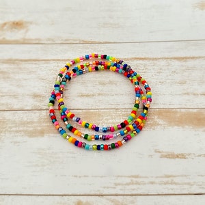 Könnte beinhalten: Mehrfarbiges Perlenarmband mit einer Vielzahl von Farben, darunter Rot, Orange, Gelb, Grün, Blau, Lila und Silber. Das Armband besteht aus kleinen, runden Perlen und ist in einem kreisförmigen Muster geschichtet.