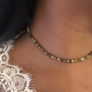 May include: A delicate choker necklace made with small, multi-coloured beads in shades of brown, gold, and green.