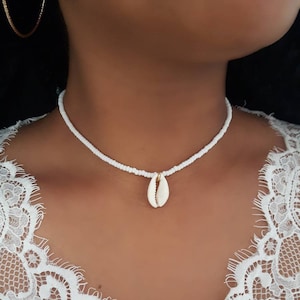 May include: A white beaded choker necklace with a small white seashell pendant.