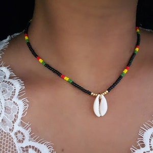 Puede incluir: Un collar de cuentas negras con detalles rojos, amarillos y verdes y un colgante de concha blanca.