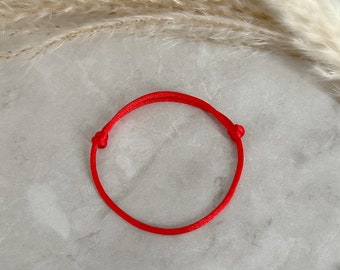 Könnte beinhalten: Ein einfaches rotes Armband aus Schnur, an beiden Enden mit einem Knoten gebunden.