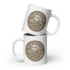May include: Two white ceramic mugs stacked. Each mug has a brown circular design with the text "Holy Grail Alehouse" and "Harmless Bunny Brew". The design includes a cartoon bunny and the words "Dynamite Flavour".