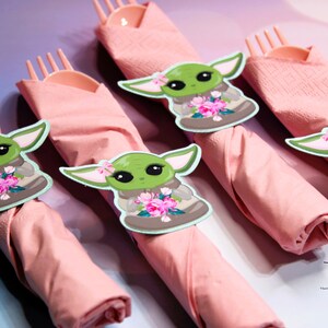 Puede incluir: Servilletas rosas con anillos de servilleta con el personaje verde Baby Yoda. Los personajes de Baby Yoda sostienen flores rosas.