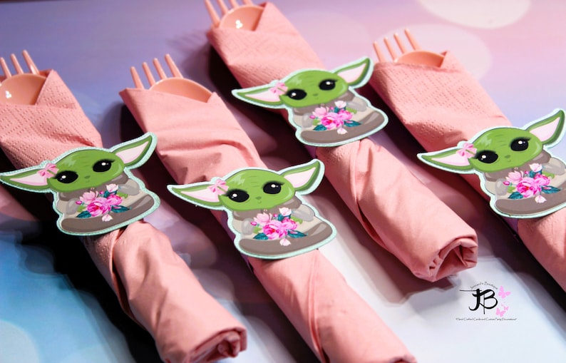 Puede incluir: Servilletas rosas con anillos de servilleta con el personaje verde Baby Yoda. Los personajes de Baby Yoda sostienen flores rosas.