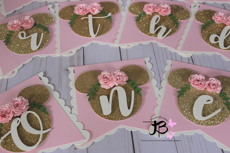 Puede incluir: Bandera de brillo rosa y dorado con letras blancas que deletrean la palabra "one". Cada letra est&aacute; decorada con una flor rosa y hojas verdes.