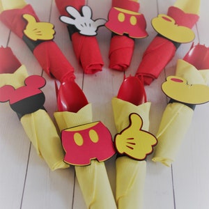 May include: Arrangement of red and yellow napkins, each holding a red spoon. The napkins are decorated with Mickey Mouse-themed cutouts, including gloves, shorts, and ears. Ideal for a themed party.