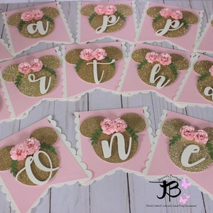 Puede incluir: Bandera de brillo rosa y dorado con las letras "Happy Birthday" en blanco. Cada letra est&aacute; en una bandera separada con un fondo rosa y una cabeza de Mickey Mouse de brillo dorado con flores rosas.