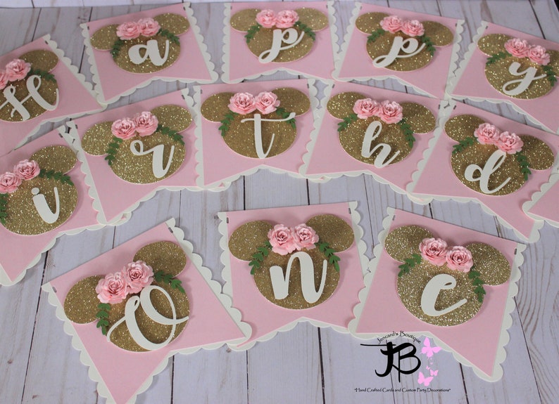 Puede incluir: Bandera de brillo rosa y dorado con las letras "Happy Birthday" en blanco. Cada letra est&aacute; en una bandera separada con un fondo rosa y una cabeza de Mickey Mouse de brillo dorado con flores rosas.