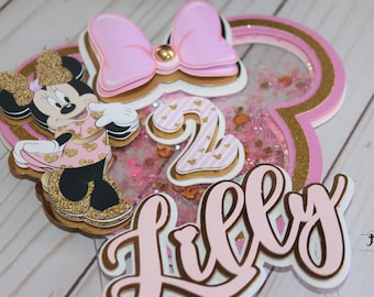 Könnte beinhalten: Rosa-goldener Minnie Mouse-Tortenaufsatz mit Glitzerhintergrund, der Zahl 2 und dem Namen "Lilly" in Kursivschrift.