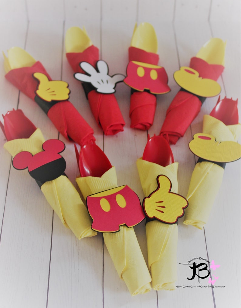 May include: A collection of party decorations featuring red napkins with yellow spoons, adorned with Mickey Mouse-themed cutouts. The decorations include Mickey's gloves, shorts, and head shapes, perfect for a themed party.