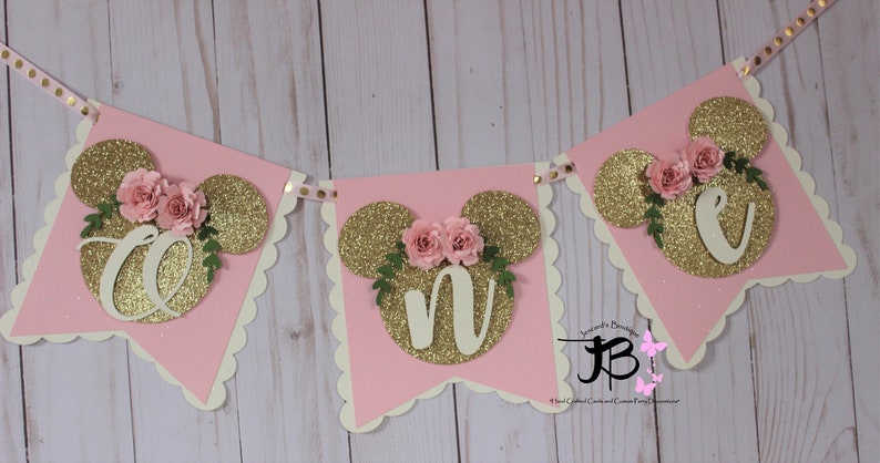 Puede incluir: Bandera de brillo rosa y dorado con las letras "ONE" en brillo dorado, cada letra est&aacute; decorada con una flor rosa y hojas verdes. La bandera es perfecta para una fiesta de primer cumplea&ntilde;os.