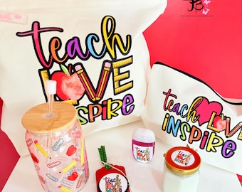 Peut inclure: Ensemble de cadeaux sur le thème de l'enseignant, comprenant un sac fourre-tout, une trousse de maquillage, un gobelet en verre, un désinfectant pour les mains et un petit pot. Les articles présentent les mots "Teach Love Inspire" en lettrage coloré, avec des graphiques de pommes et de crayons.