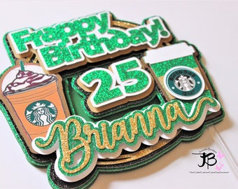 May include: Green and gold glitter cake topper with the words "Happy Birthday!" and "Brianna" and the number "25". The topper also features two coffee cups with a Starbucks logo.