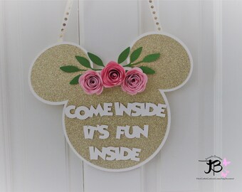 May include: Gold glitter Mickey Mouse shaped door hanger with pink paper flowers and green leaves. The text "Come Inside It's Fun Inside" is written in white letters.