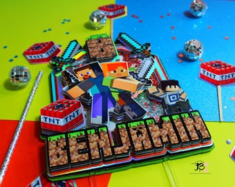 Op de afbeelding: Een Minecraft-thema caketopper met een groen en blauw personage, rode en zwarte TNT-blokken en de naam "Benjamin" in bruine gepixelde letters.