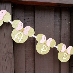 May include: Gold and pink Minnie Mouse themed banner with the word "Happy" spelled out. Each letter is on a separate Minnie Mouse head with a pink bow.