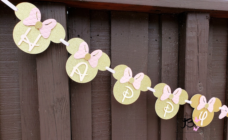 May include: Gold and pink Minnie Mouse themed banner with the word "Happy" spelled out. Each letter is on a separate Minnie Mouse head with a pink bow.